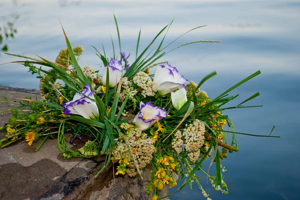 One beautiful big bouquet of a wreath of fresh wildflowers and green grass lies on the rocks of a parapet wall of rocks against the background of the Ukrainian river Dnepr on the feast of Ivan Kupala