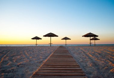 büyük plaj şemsiyeleri çeşitli bir sürü saman ve metal stand ahşap yol kum plaj mavi deniz mavi gökyüzü yaz sabah akşam sakin deniz kıyısında iz üzerinde yapılan