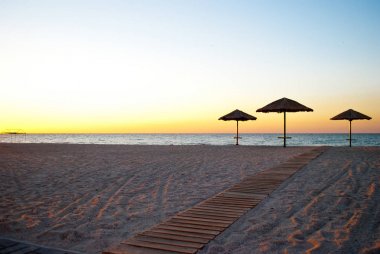 büyük plaj şemsiyeleri çeşitli bir sürü saman ve metal stand ahşap yol kum plaj mavi deniz mavi gökyüzü yaz sabah akşam sakin deniz kıyısında iz üzerinde yapılan