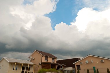 Beyaz güzel kabarık büyük bulutlar gri yağmur fırtına fırtına mavi gökyüzü ile farklı renkli evleri altında bir arka plan üzerinde güzel manzara yaz günü yağmur önce çatılar