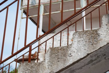 Beton merdiven, paslı korkuluk, terk edilmiş bir binada, mavi gökyüzünün ve ahşap arka plan üzerinde tuğla bina çatı üzerinde