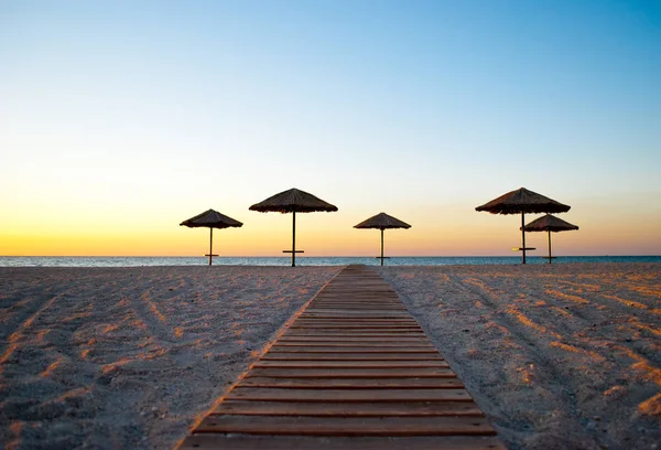 büyük plaj şemsiyeleri çeşitli bir sürü saman ve metal stand ahşap yol kum plaj mavi deniz mavi gökyüzü yaz sabah akşam sakin deniz kıyısında iz üzerinde yapılan