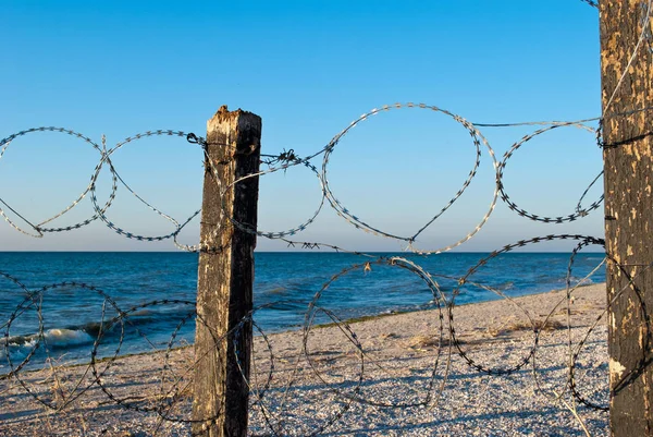 barbed wire mesh of metal and pillars of wood protects a deserted beach fence passage banned yellow sand blue sea shore clear blue sky summer warmth
