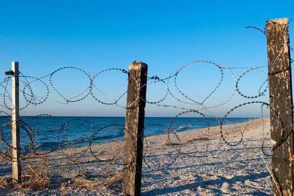 barbed wire mesh of metal and pillars of wood protects a deserted beach fence passage banned yellow sand blue sea shore clear blue sky summer warmth