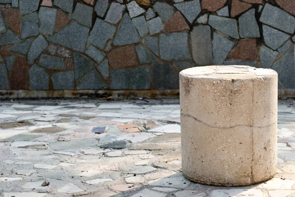 A low concrete stone pillar, on the right in the photo, against a background of a large stone tile texture, a mosaic, a bright summer sunny day