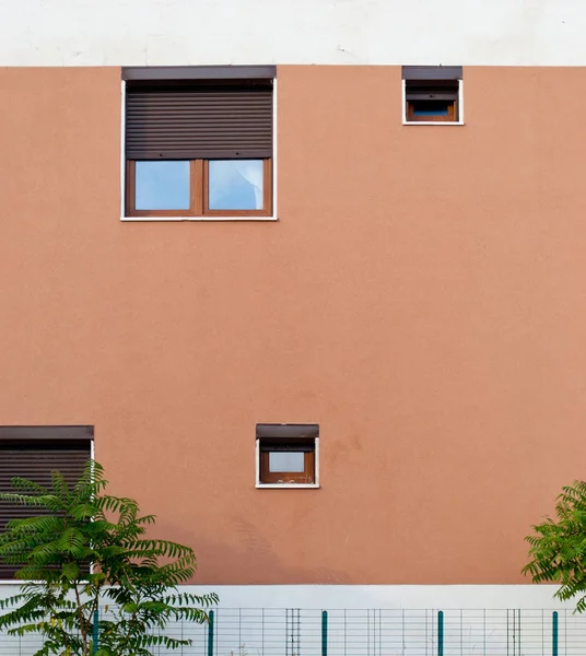 Windows, farklı boyutlarda, orada Stor perde ile evin duvarına gökyüzü bir yansımasıdır, aşağıda bir metal çit, yeşil ağaç çalılar, mimari