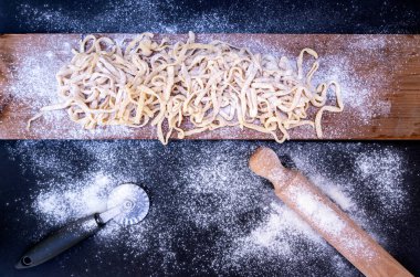 Tahta masada çiğ makarna ve merdane makasıyla.