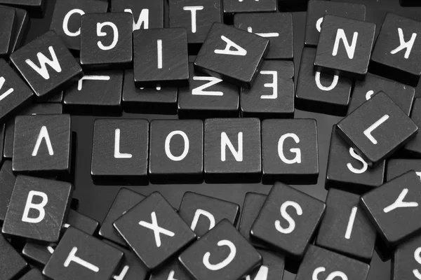 Schwarze Buchstaben Kacheln buchstabieren das Wort "lang" — Stockfoto