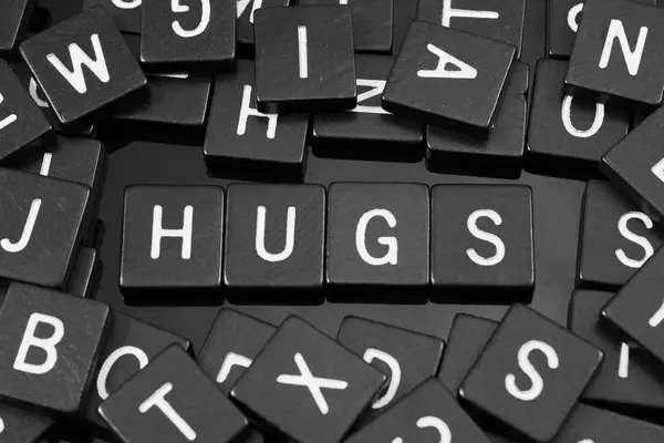 Azulejos de letras negras deletreando la palabra "abrazos " — Foto de Stock