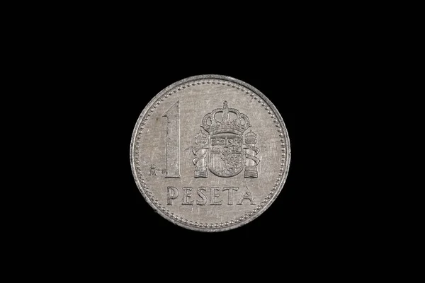 An old Spanish one peseta coin featuring Rey Juan Carlos, shot close up in macro, on a black background