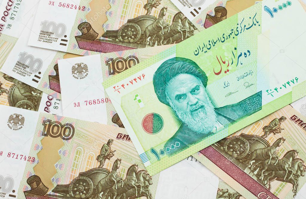 A macro image of a green ten thousand rial bank note from Iran on a bed of Russian one hundred ruble bank notes close up