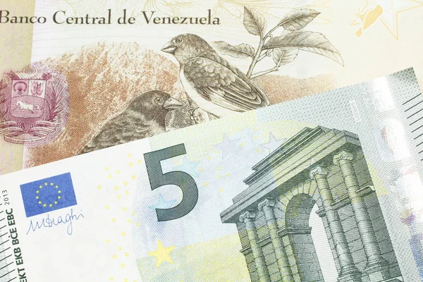 A one hundred Bolivar note from Venezuela with a five Euro note from the European Union eurozone close up in macro
