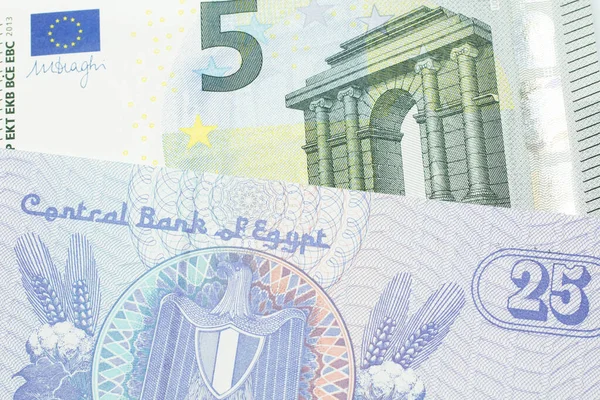 A close up image of a purple, twenty five Egyptian piastres note close up in macro with a blue and green, European five euro bank note