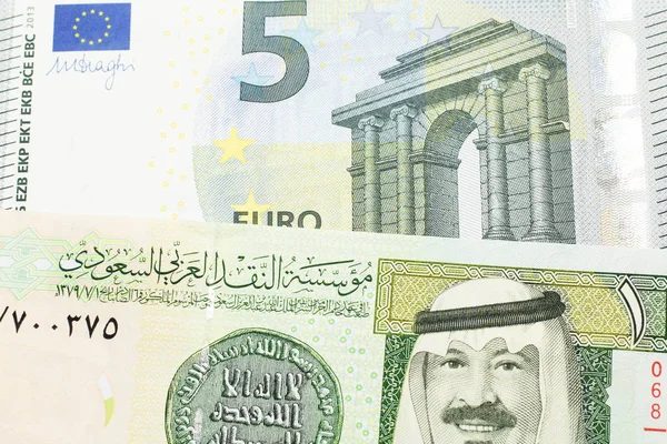 A green one riyal bank note from Saudi Arabia with a blue and green five euro bank note close up in macro