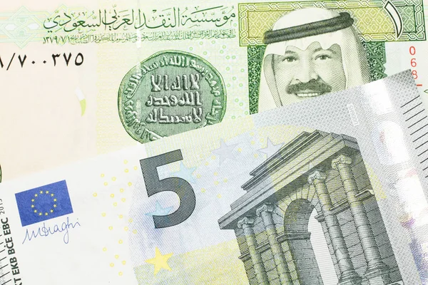 A green one riyal bank note from Saudi Arabia with a blue and green five euro bank note close up in macro