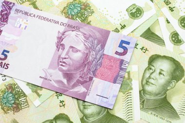 Brezilya 'dan gelen pembe bir 5 reais banknotu Çin yuan banknotlarının arka planında makro olarak kapanıyor.