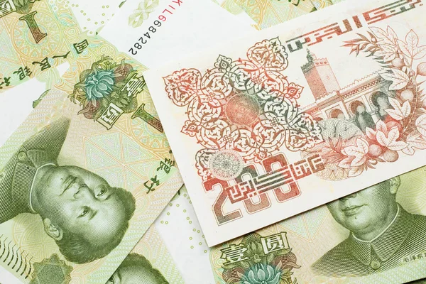 A macro image of a beige two hundred Algerian dinar bank note on a background of Chinese one yuan bank notes