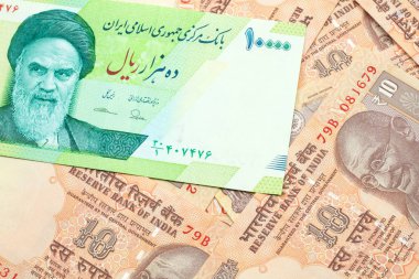 A macro image of a green ten thousand rial bank note from Iran on a bed of Indian ten rupee bank notes close up