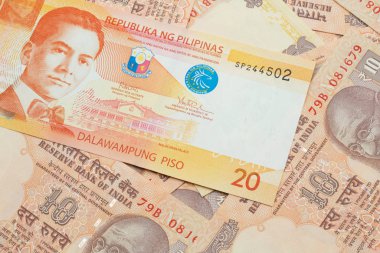 An orange twenty piso bank note from the Philippines with Indian ten rupee bank notes close up in macro