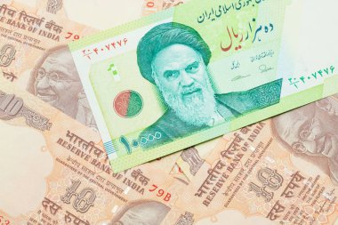 A macro image of a green ten thousand rial bank note from Iran on a bed of Indian ten rupee bank notes close up