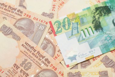 A close up image of a twenty shekel bank note from Israel on a background of Indian ten rupee bank notes in macro