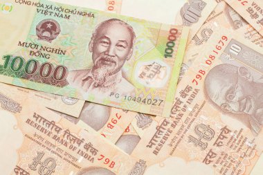 A close up image of a Vietnamese ten thousand dong bank note on a background of Indian ten rupee bank notes in macro
