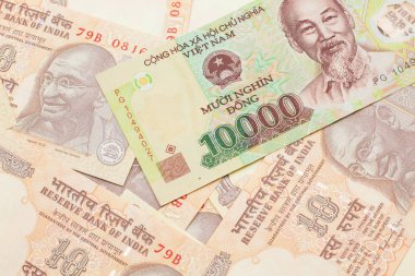 A close up image of a Vietnamese ten thousand dong bank note on a background of Indian ten rupee bank notes in macro
