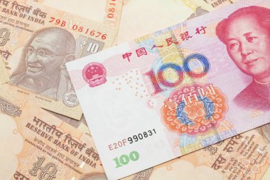 A close up image of a red, one hundred Chinese yuan bank note, close up on a background of orange Indian ten rupee bank notes.  Shot in macro