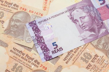 A pink five reais bank note from Brazil close up in macro with a background of Indian rupee bills