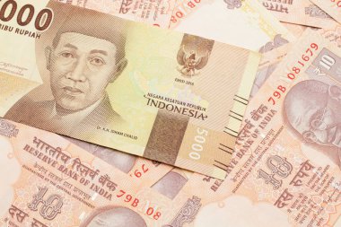An orange, five thousand Indonesian rupiah bank note with Indian ten rupee bank notes close up in macro