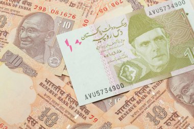 A close up image of an orange and ten Pakistani rupee bank note with Indian twenty rupee bank notes in macro