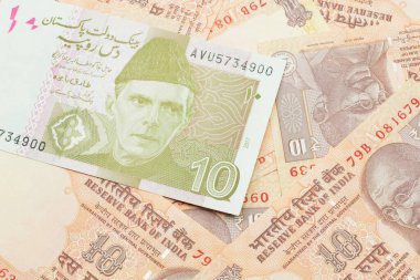 A close up image of an orange and ten Pakistani rupee bank note with Indian twenty rupee bank notes in macro