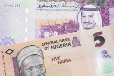Nijerya 'dan beş nairalık şeftali rengi bir banknot ve makroda beş adet Suudi riyal banknotu.