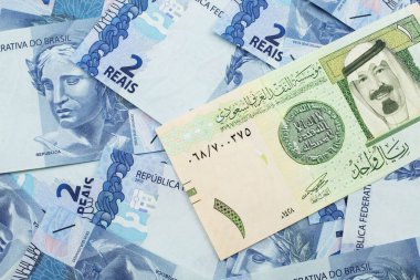 Suudi Arabistan 'dan gelen bir riyal banknotunun yakın plan resmi makrodaki iki reais banknotunun arka planında.