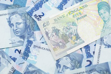 Birleşik Krallık 'tan gelen çok renkli beş sterlinlik banknotun yakın plan resmi makroda Brezilya' nın iki reais banknotunun arka planında