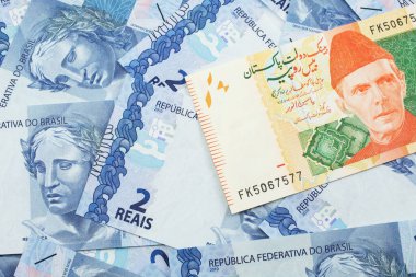 Turuncu ve yeşil bir resim 20 Pakistan rupi banknot ve makroda iki reais banknot