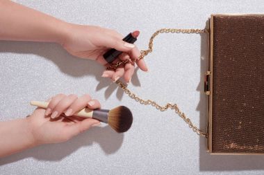 Makyaj ürünleri ve debriyaj çanta çanta glitter arka planda tutan kadının kolları