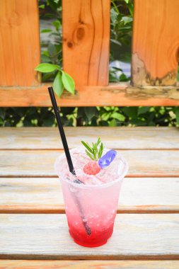 Çilekli İtalyan gazozu, kelebek bezelyesi çiçekli, plastik bardakta, ahşap masada..