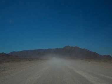 Açık mavi gökyüzü ile çöl manzara arasında kayalık dağa tozlu asfaltsız yol üzerinden sürüş