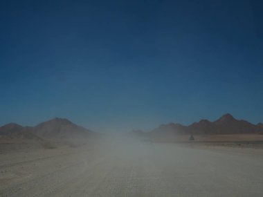 Açık mavi gökyüzü ile çöl ve dağ manzara arasında puslu asfaltsız yol üzerinden yolculuğa offroad araç sürüş