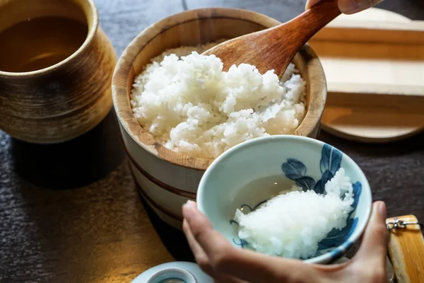 Närbild ångade japanska vitt ris i traditionella träskål med tjänande händer och träbord bakgrund — Stockfoto