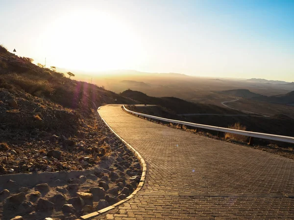 Driving offroad car on adventure road trip through proper block paved curved road among dried desert and rock mountain landscape to dusty vast horizon on beautiful sunshine day — Stock Photo, Image