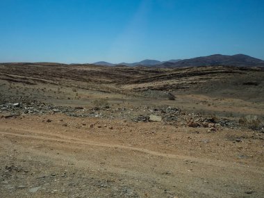 Araba lastik parça kuru çöl iklim ve hard rock dağ manzarası açık mavi gökyüzü ile aracılığıyla ile zor tozlu asfaltsız yol aracılığıyla yolculuk