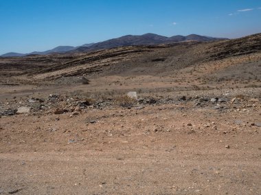 Araba yolculuğu zorlu tozlu asfaltsız yol araba lastik ile aracılığıyla takip yoluyla kuru çöl iklim ve hard rock dağ manzara arka plan açık mavi gökyüzü ile