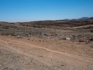 Araç Lastik ile zorlu tozlu asfaltsız yol yol yolculuk izlemek kuraklık çöl iklim ve hard rock dağ manzara arka plan açık mavi gökyüzü ve kurutulmuş plan aracılığıyla