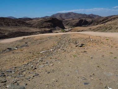 Namib Çölü benzersiz coğrafyasının taş zemin road, çöl bitki ve açık mavi gökyüzü bölme ile manzara arka astar büyük rock dağ dokusu ile yolculuk