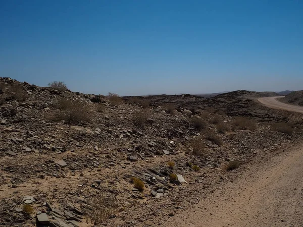 Przygody podróż scena na brud podróż przez pustynia Namib suszy krajobraz góry horyzont z lokalnych roślin, łupania kamienia i błękitne niebo — Zdjęcie stockowe