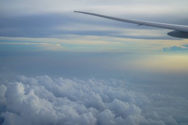 Kabarık soyut beyaz bulut ve mavi gökyüzü ile uçağın kanat ve gündoğumu açık renkli uçak penceresinden görünümü