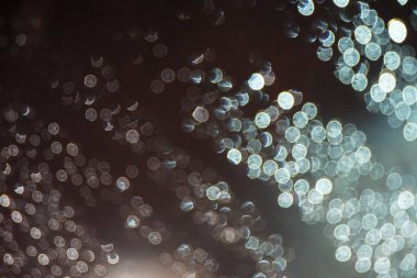 Geceleri araba penceresinde dağınık degrade ışık ile karanlık siyah arka plan üzerine yağmur damlası ufuk şenlikli beyaz ışık bokeh noktalardan soyut