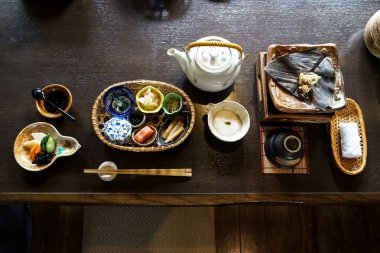 Japon ryokan kahvaltı iştah açıcı bulaşıkları mentaiko, turşu, deniz yosunu, bambu ateş, sıcak sac, diğer yan yemekler, yeşil çay potu, kupa ve ahşap masa üzerine sıcak havlu dahil